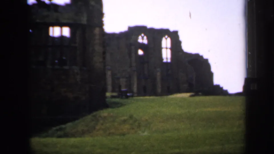 1949 England 8mm frame showing a closer pan view of stone ruins, bright Gothic windows, and a low green mound in front.