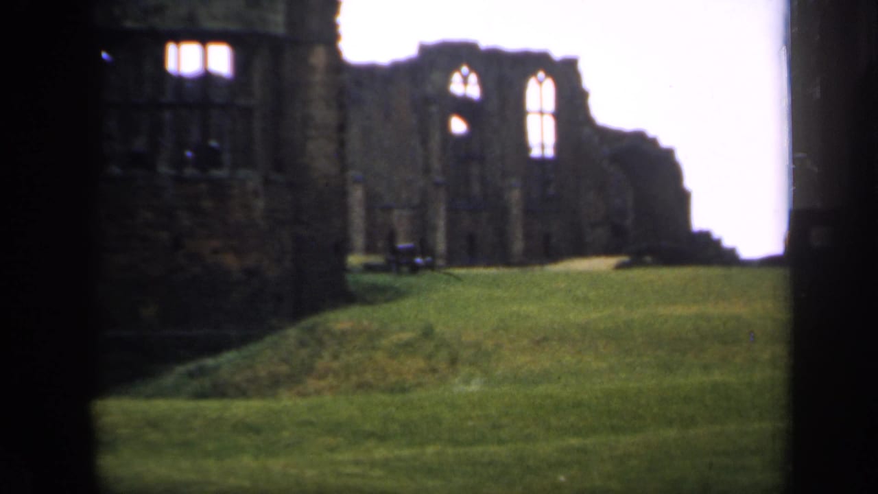 Ruined stone building with arched windows above a grassy slope.