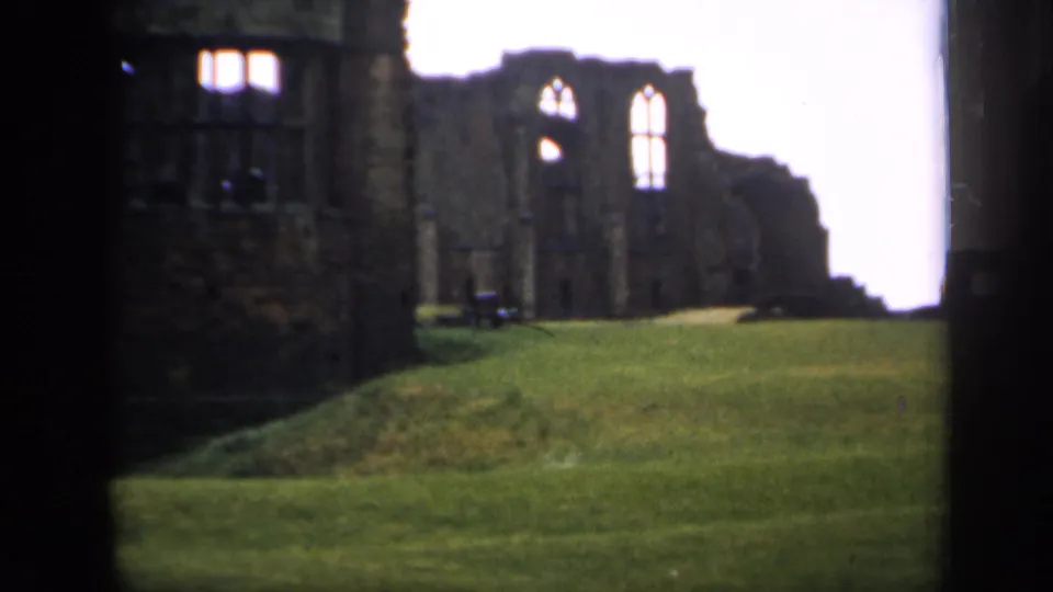 1949 England home-movie frame showing castle-like stone ruins, tall window openings, and a green lawn in soft 8mm focus.