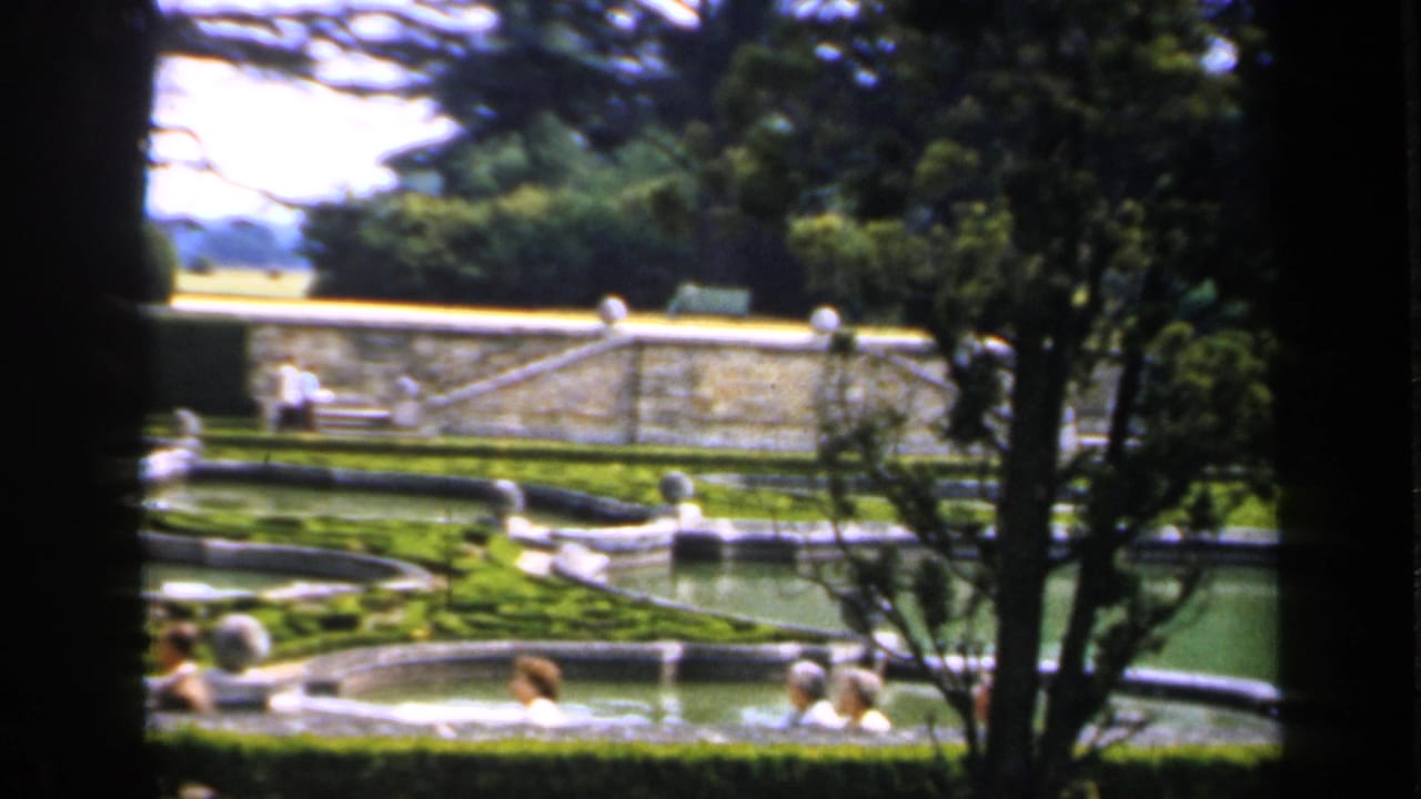 Formal garden pools and hedges seen through dark foreground framing.