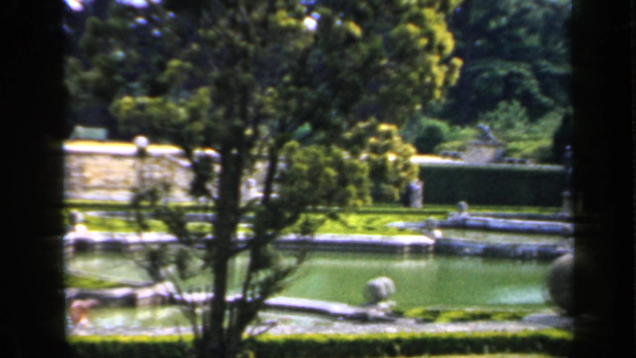 Garden fountain pools with hedges, trees, and distant people.