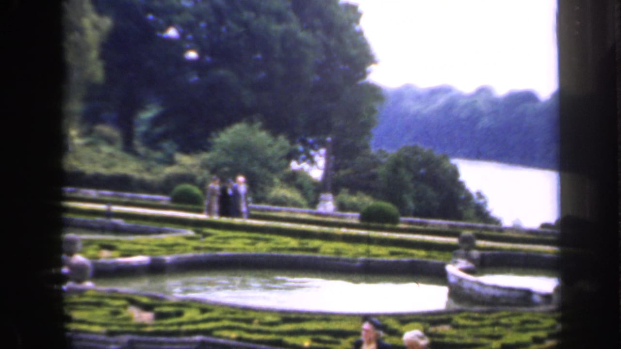 1949 England garden view with formal hedges, a stone fountain basin, visitors on the terrace, and a broad river beyond the trees.
