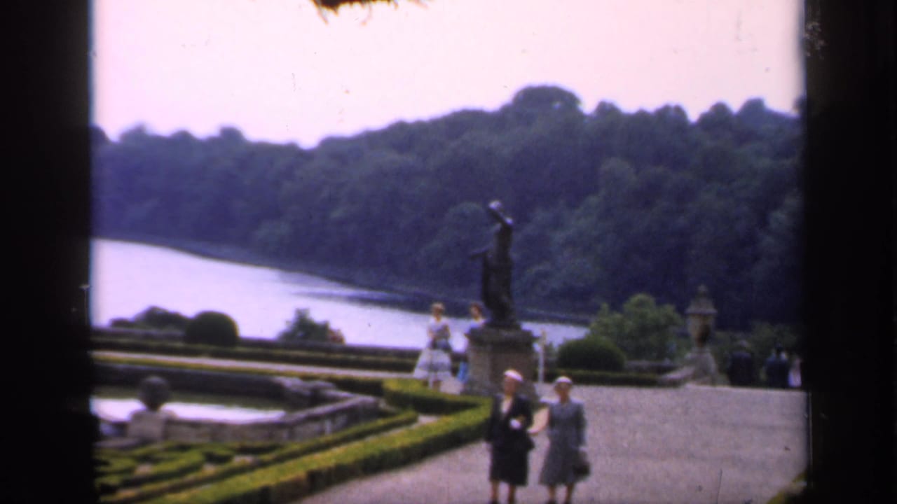 Garden overlook with statue, water, hedges, stonework, and several visitors.