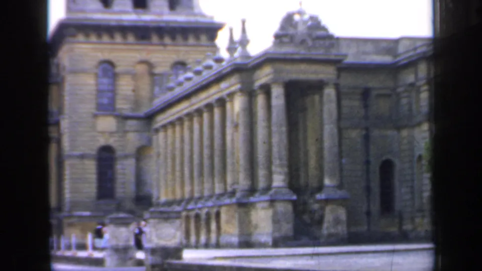 1949 England view of the building's long colonnaded side, with arched windows, stone detailing, and small distant figures near the foreground.