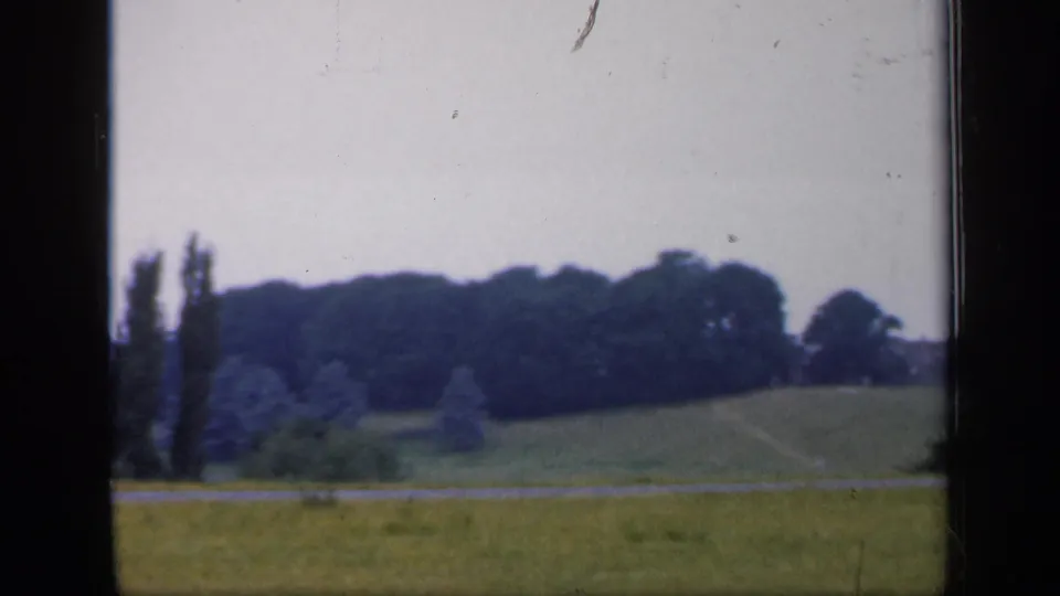 1949 England rural landscape frame with open pasture, a distant low hill, tall trees, and no visible people or buildings.