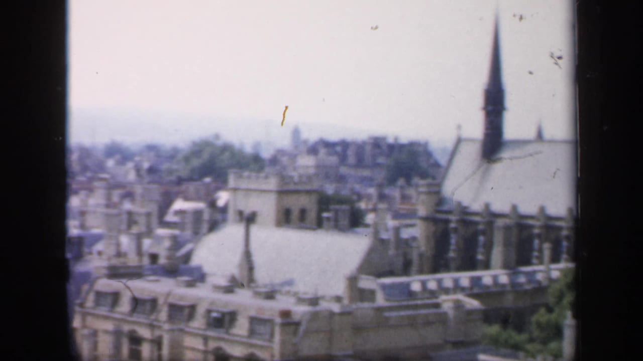 1949 England elevated view over rooftops toward a historic church with a tall spire and hazy town background.