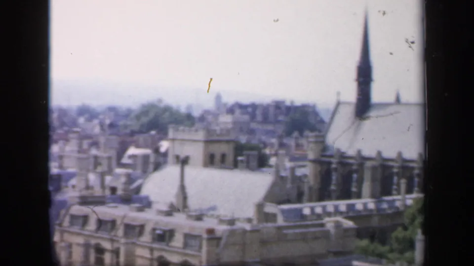1949 England elevated view over rooftops toward a historic church with a tall spire and hazy town background.