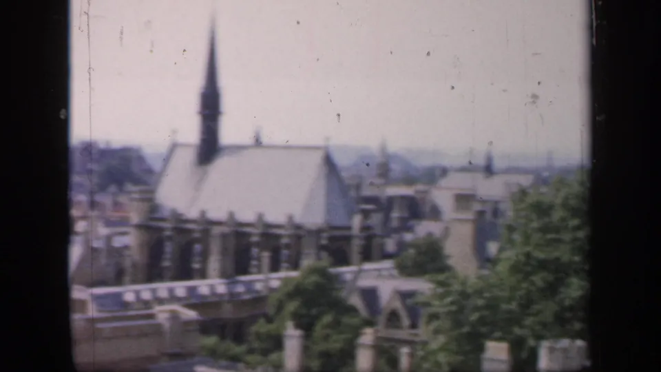 1949 England home-movie view of a church roof and tall spire rising above nearby town buildings.