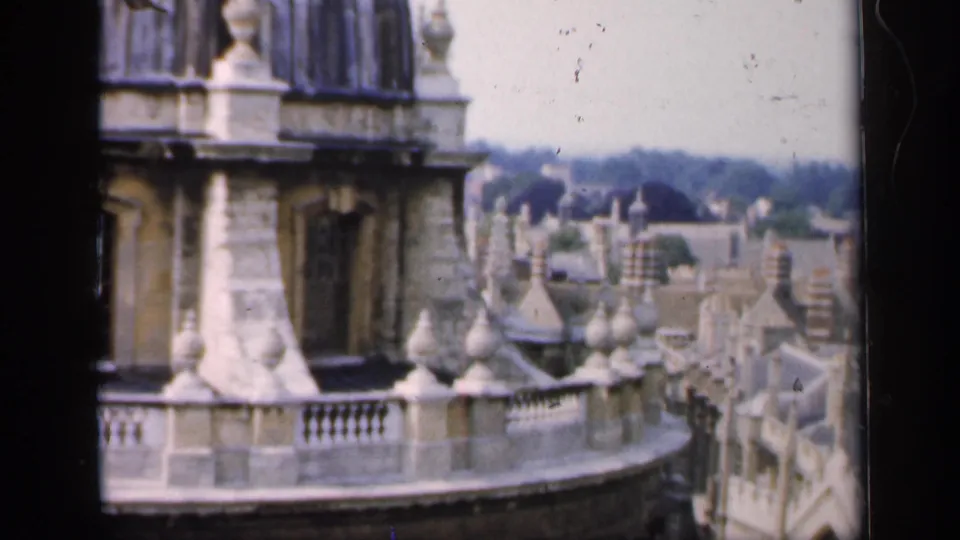1949 Oxford view with a stone building edge in the foreground and a dense roofline of historic university buildings beyond.