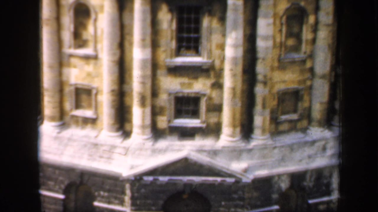 Stone building facade with columns, arched openings, windows, and dark masonry base.
