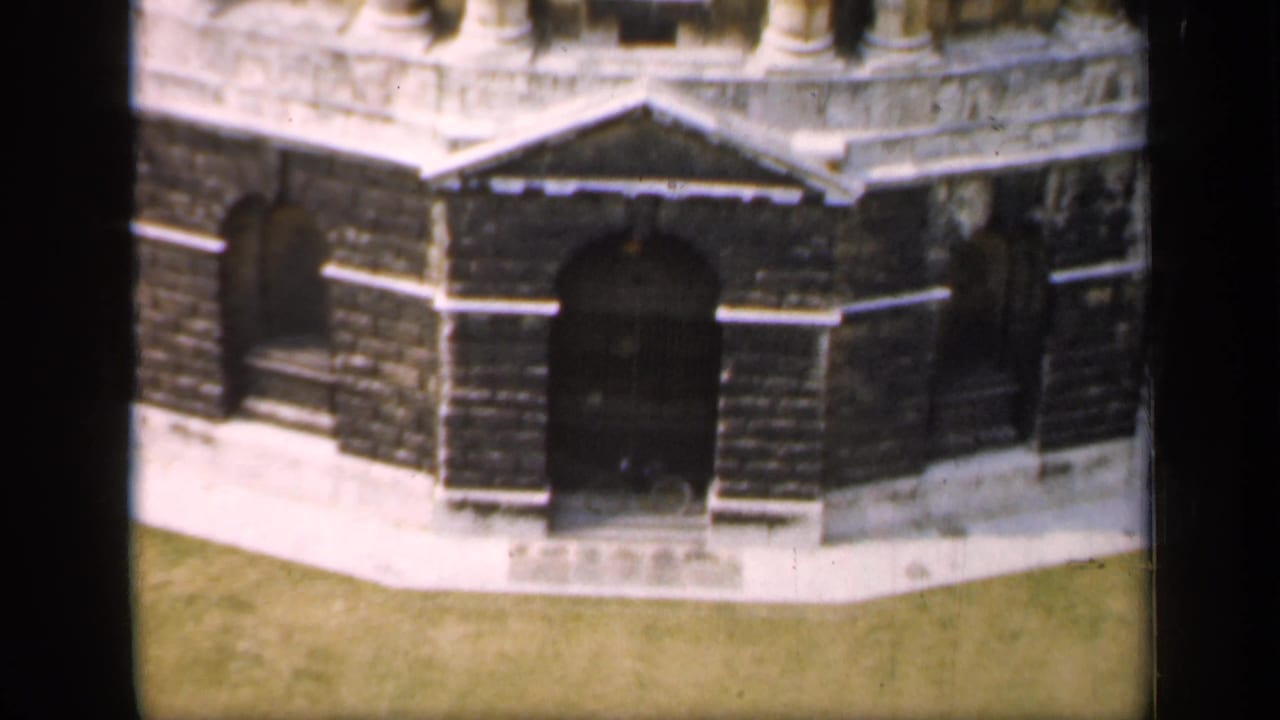 Lower section of a stone building with arched doorway, dark masonry, and grass in front.