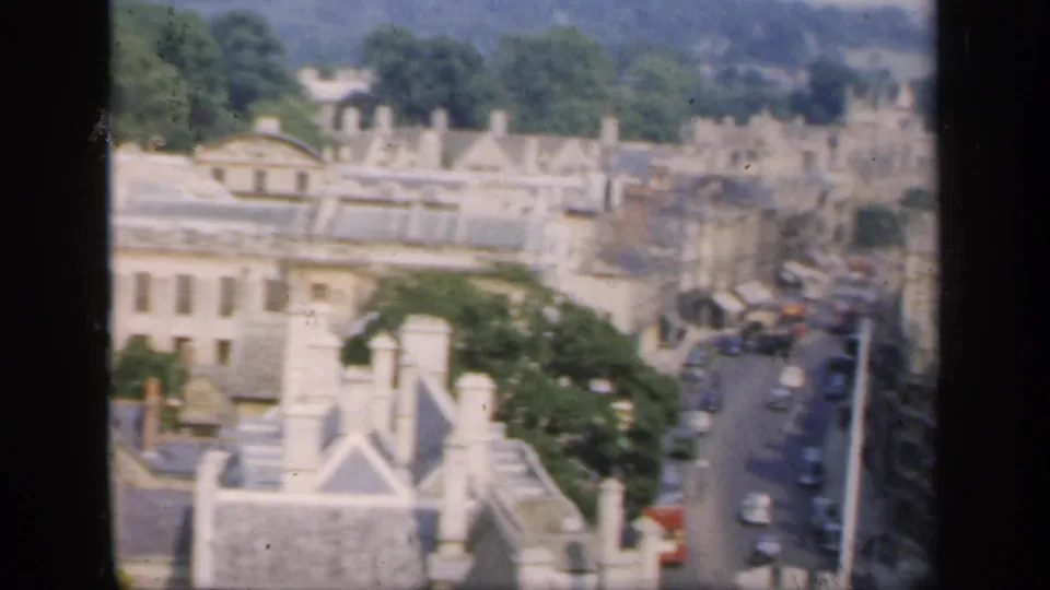1949 England 8mm frame with an elevated view over rooftops, trees, and a village street with cars.