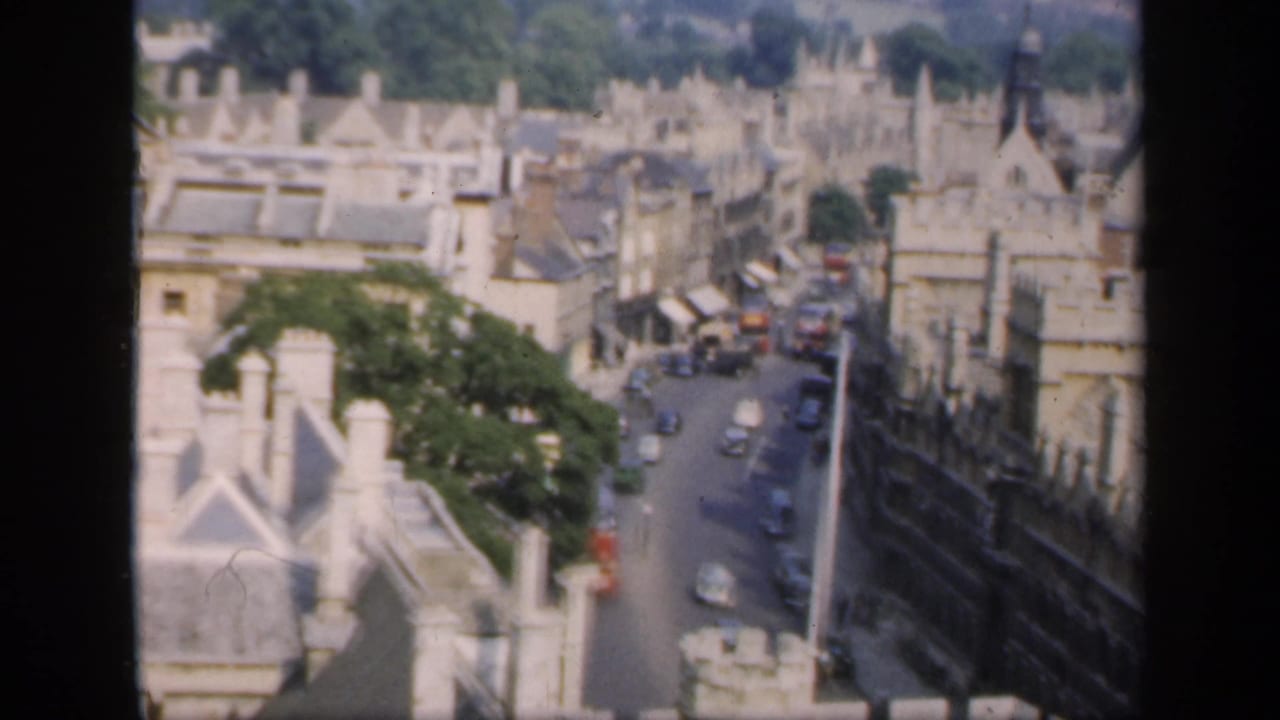 High-angle view over pale stone buildings and a narrow street with cars.