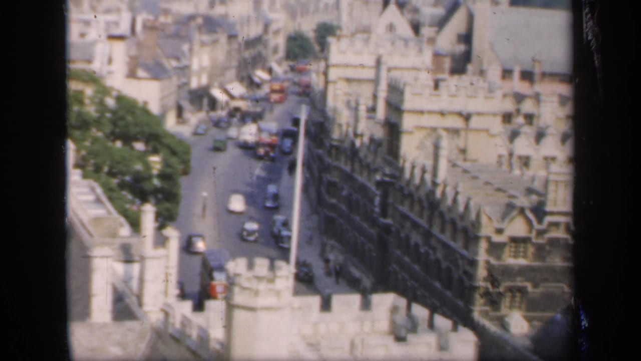 1949 8mm view from above an English town, showing a narrow street, stone architecture, rooftops, and period vehicles.