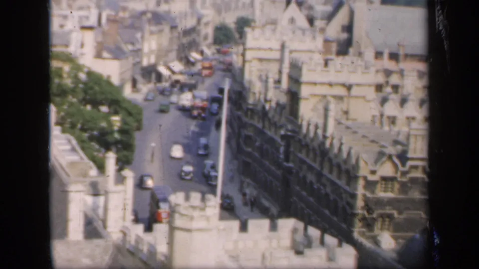 1949 8mm view from above an English town, showing a narrow street, stone architecture, rooftops, and period vehicles.