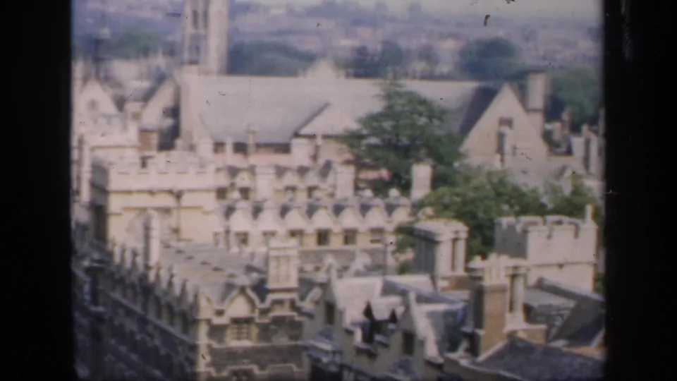 Elevated 8mm frame of an English town in 1949, centered on ornate stone buildings, roofs, chimneys, and trees.