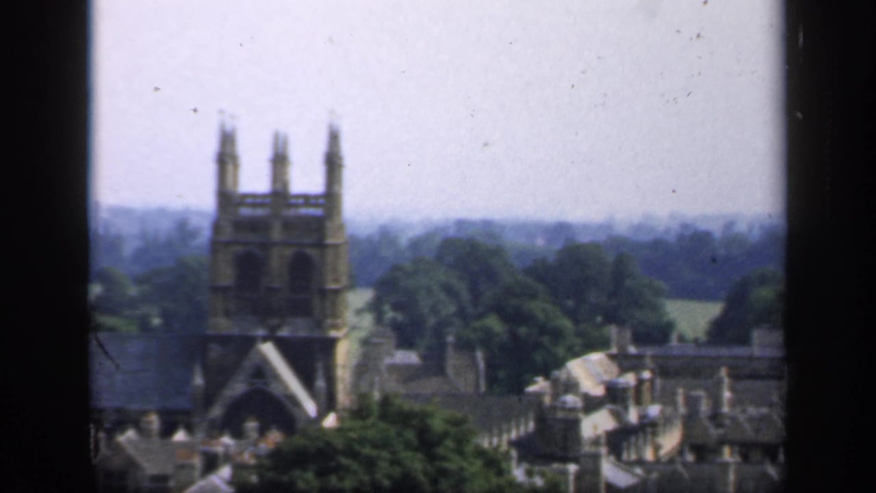 Church tower, rooftops, trees, and distant fields viewed from above.