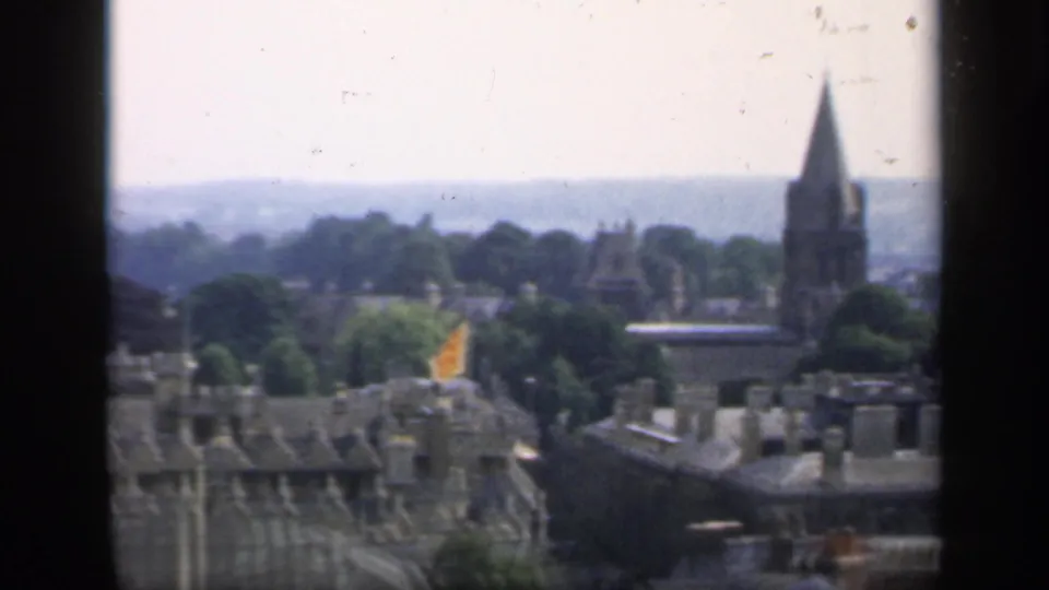 Final 1949 England view across rooftops and trees toward a pointed church spire and pale hills under a hazy sky.
