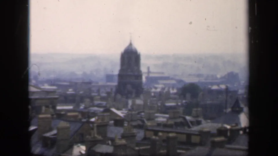 Final 1949 8mm city panorama frame showing an English rooftop foreground, a domed tower, distant haze, and a dark vertical frame edge.