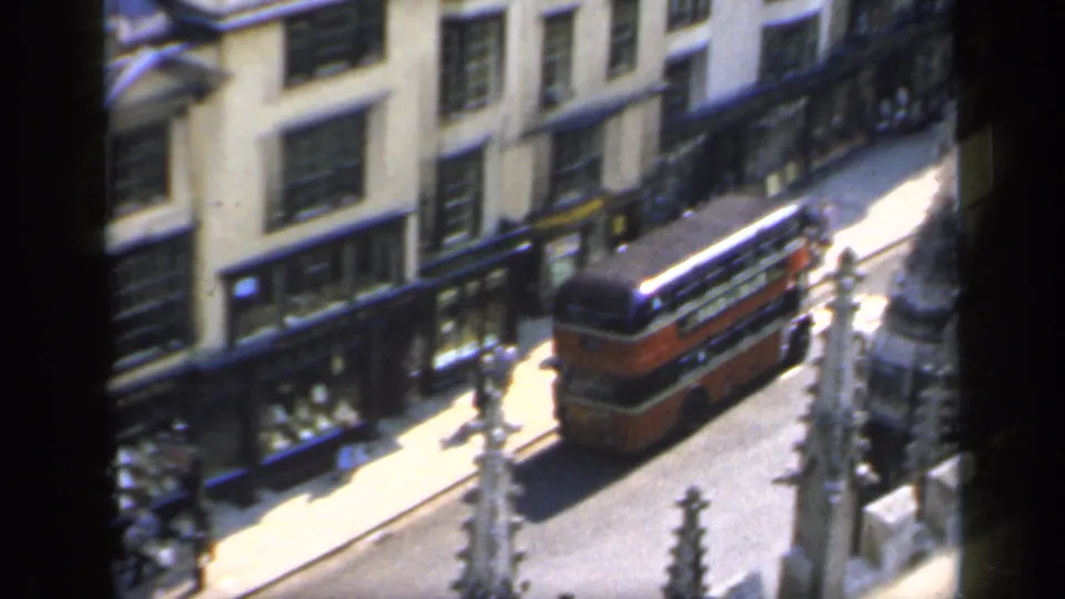1949 England street view with a red double-decker bus, pedestrians, and commercial-looking ground-floor windows.