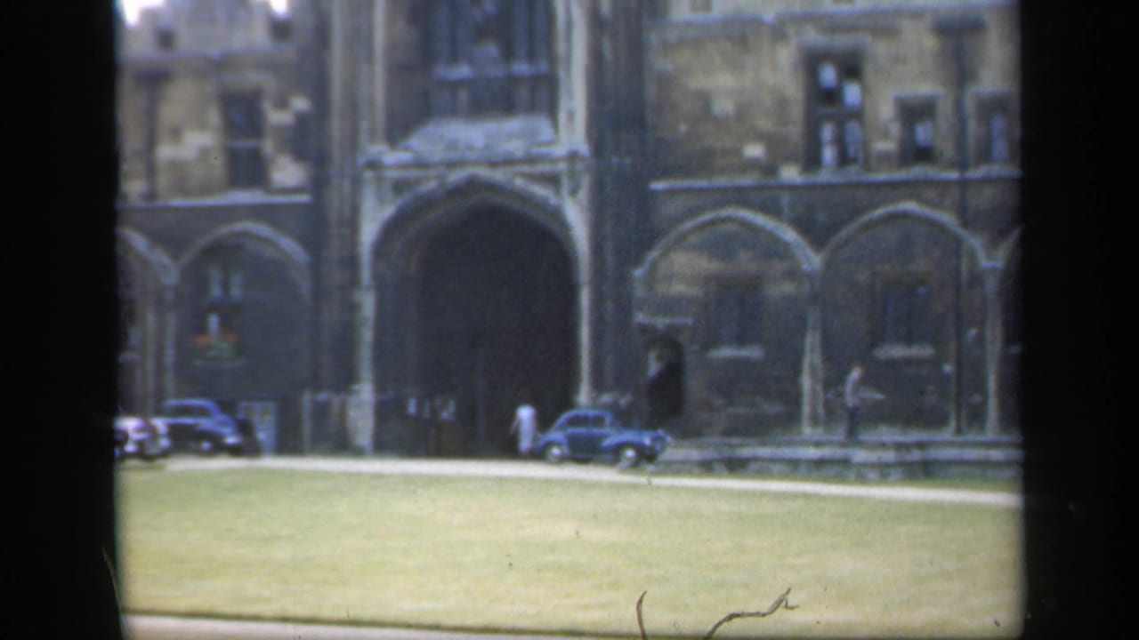 1949 England home-movie frame showing a Gothic cathedral facade, open grass, classic cars, and people near the entrance.