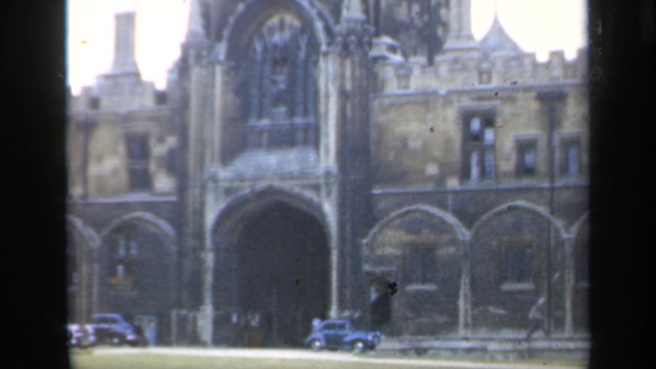 Gothic cathedral entrance in England with mid-century cars and distant pedestrians visible in a 1949 8mm frame.