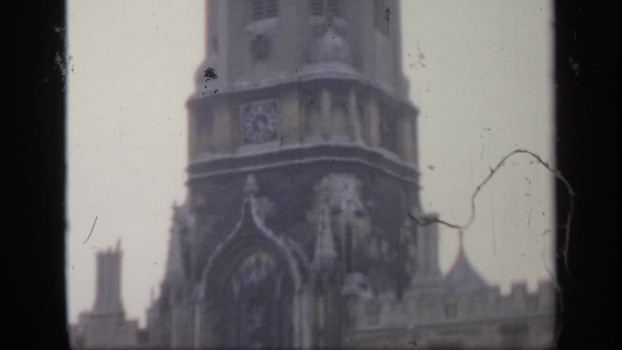 1949 England home-movie frame showing a tall stone tower and Gothic-style facade, partly obscured by dark film borders and age marks.