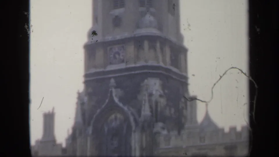 1949 England home-movie frame showing a tall stone tower and Gothic-style facade, partly obscured by dark film borders and age marks.