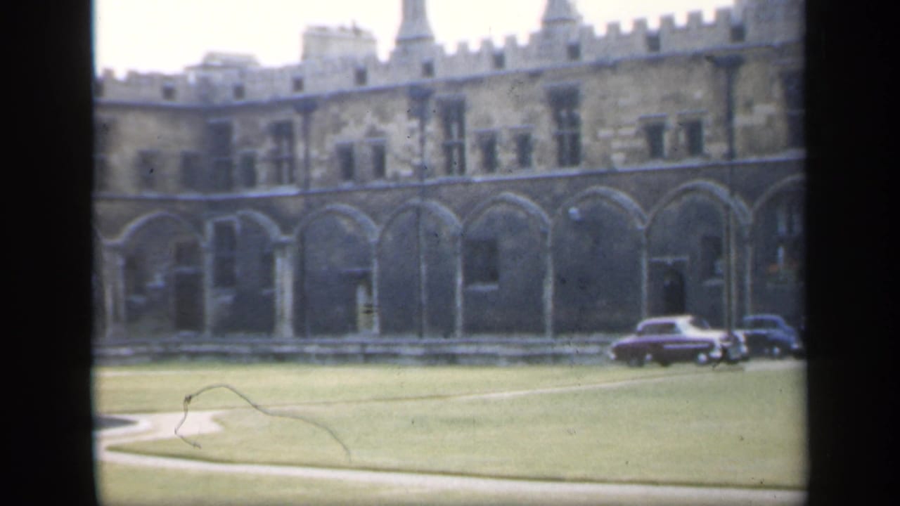 Historic stone courtyard with arched colonnade, lawn paths, and parked classic cars.