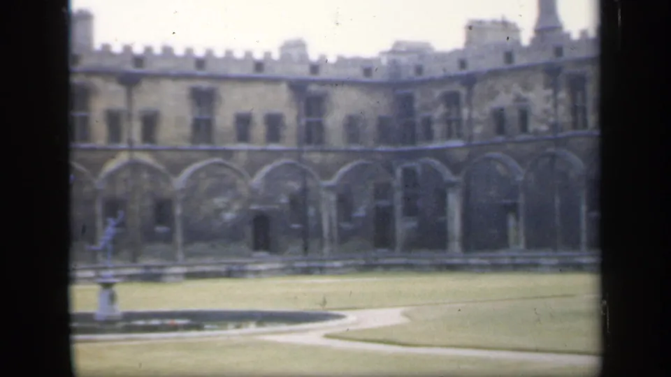1949 England frame with a central fountain statue, clipped lawn, paths, and a crenellated historic stone facade.