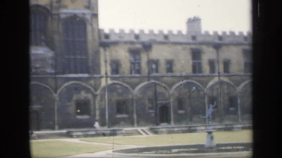 1949 England frame showing the courtyard's arched stonework, tower edge, lawn, pathways, and fountain statue.