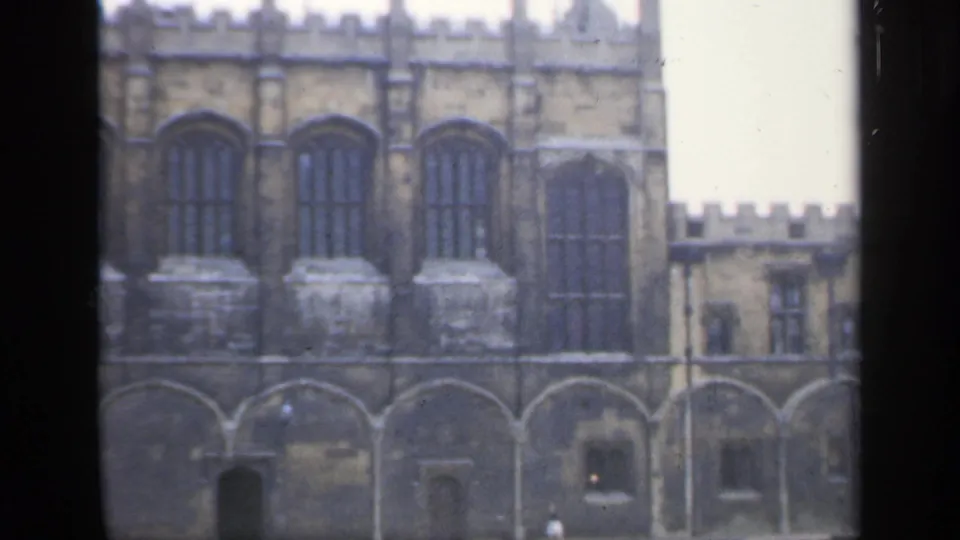 A 1949 England frame shows the upper facade of a large historic stone building with tall arched windows and crenellated battlements.