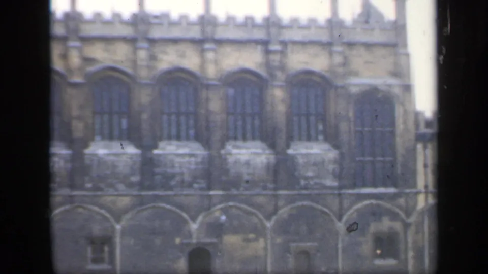 The 8mm frame records a closer view of a historic English stone facade, with repeated arched windows and lower stone arches in soft focus.