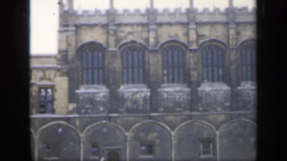 A 1949 England exterior view frames repeated arched windows, a crenellated roofline, and lower stone arches.