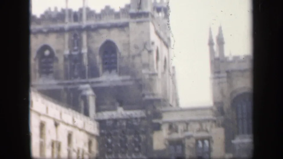 A 1949 England home-movie frame shows an angled view of Gothic-style stone architecture, battlements, and a bright gap between structures.