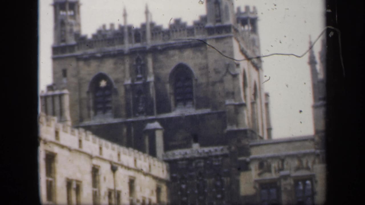 1949 England frame with a Gothic facade, crenellated towers, arched windows, and adjacent courtyard stonework.