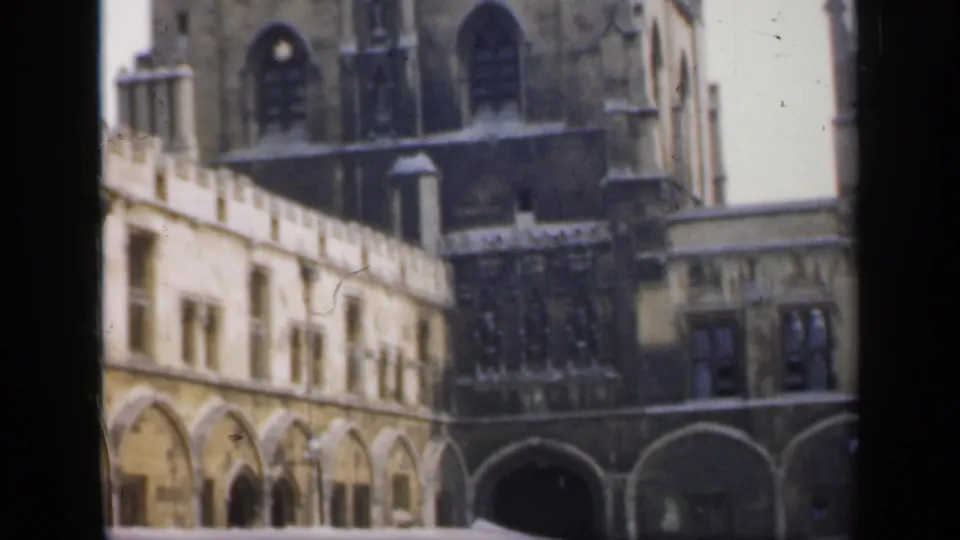 1949 England home-movie view of a stone courtyard with arcades, Gothic windows, and towers in the background.