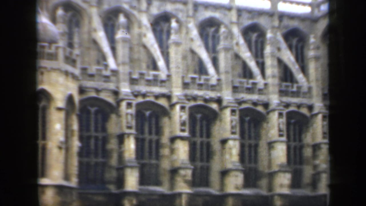 Gothic stone facade with tall arched windows and buttresses seen through dark frame edges.