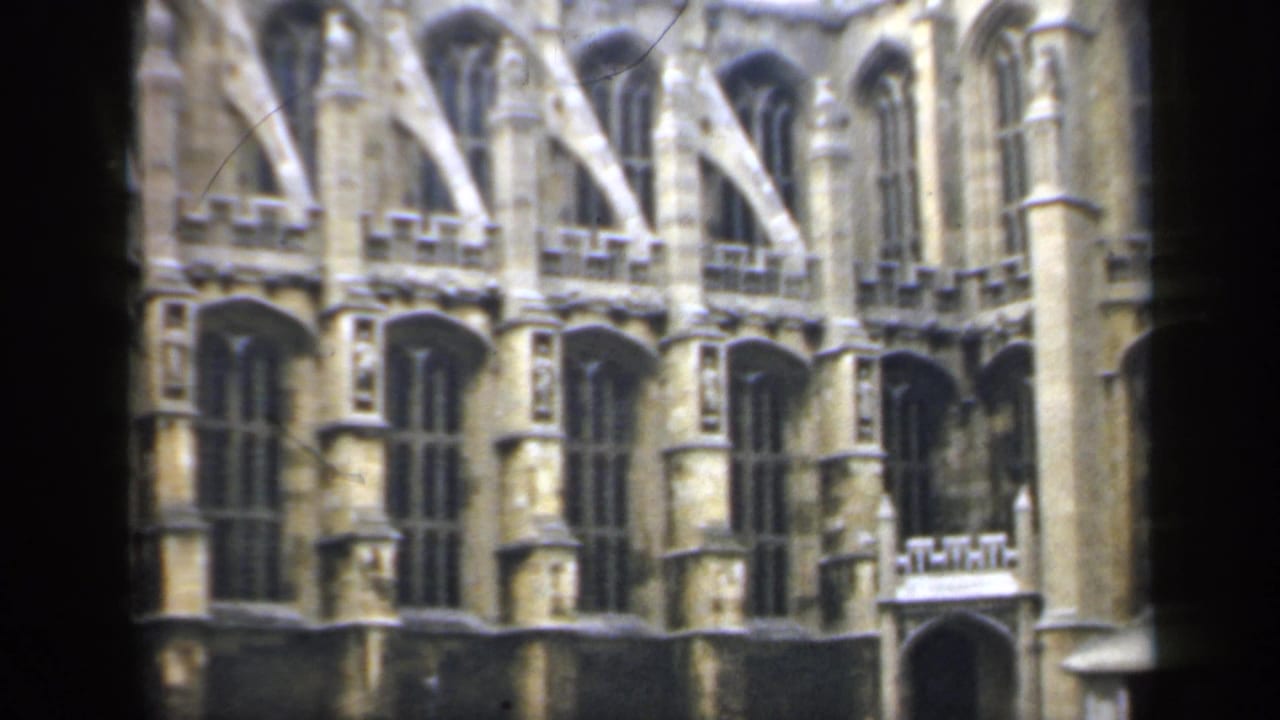 1949 England frame showing a historic stone building facade with Gothic window tracery, buttresses, and a small arched entrance detail.