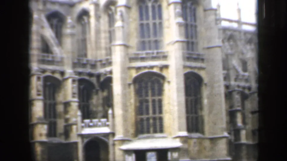 1949 England home-movie frame of a Gothic stone building corner, with tall windows, carved details, and soft 8mm exposure.