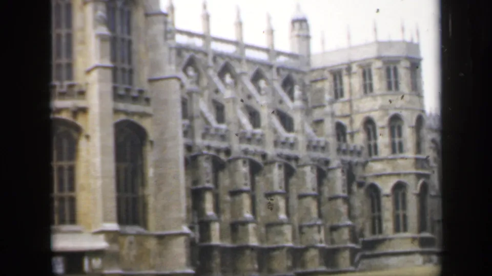 1949 England home-movie frame showing a grand Gothic stone exterior with tall windows, buttresses, and a foreground lawn.