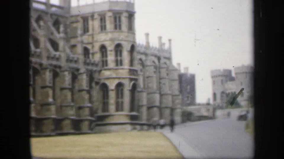 1949 England home-movie still showing the landmark corner, open grass, a road, small pedestrians, and distant cars.