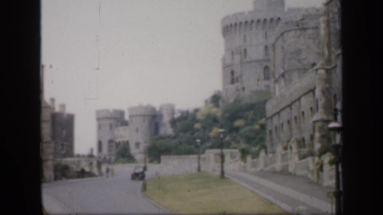 Castle walls and towers line a road with lamps, grass, and distant traffic.