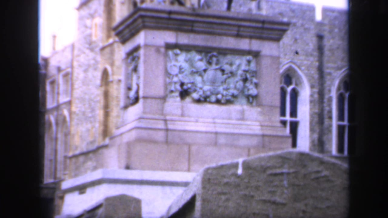 Carved stone pedestal beside Gothic-style windows and gravestones.