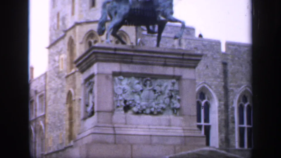 1949 England home-movie frame showing the monument pedestal, carved relief, Gothic windows, and the lower part of a horse statue.