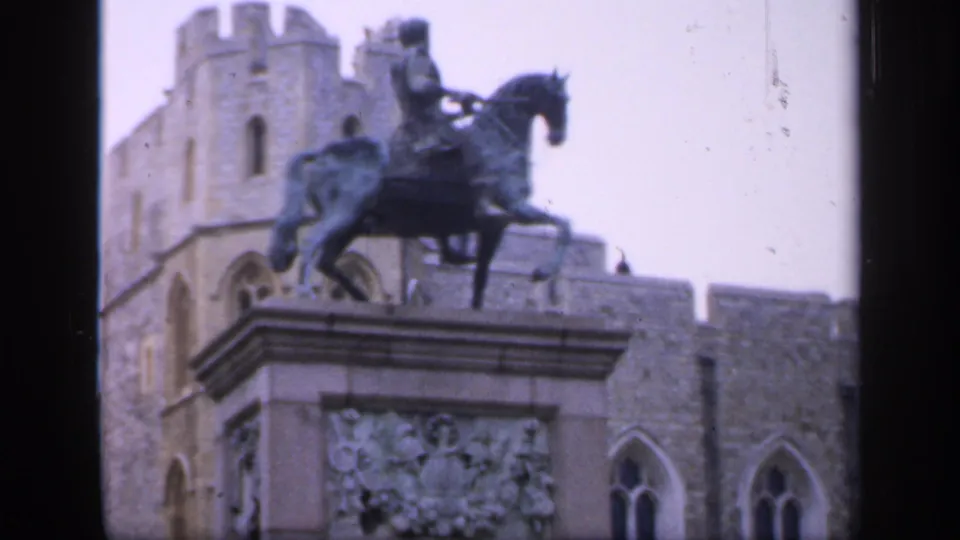 1949 England frame showing a horse-and-rider statue on a carved pedestal with Gothic-style masonry and arched windows behind it.