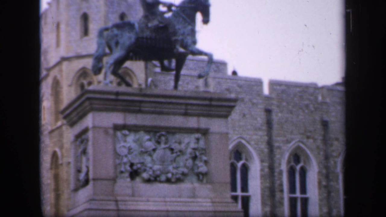 1949 England 8mm frame showing an equestrian statue beside a historic stone castle facade with Gothic arched windows.