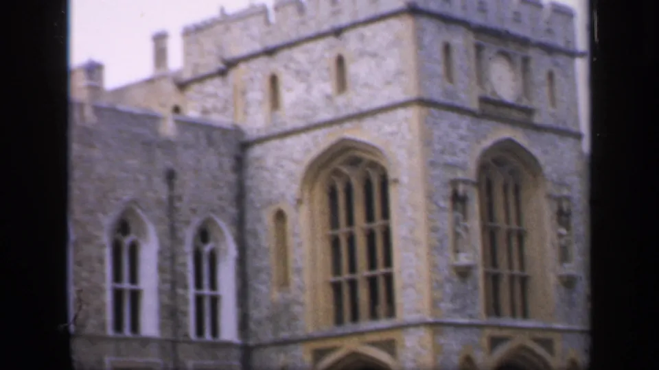 1949 England 8mm frame showing a corner of a historic stone castle with large arched windows and adjoining walls.