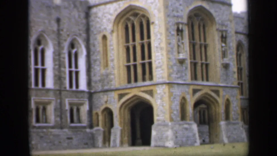 1949 England 8mm frame showing a castle entrance, tall arched windows, stone facade, and blocks near the doorway.