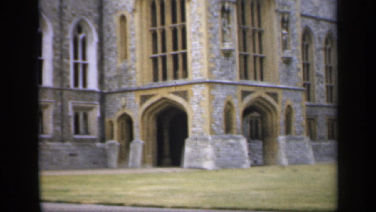 1949 England 8mm frame showing a weathered stone Gothic-style building with arched windows, doorways, and lawn in front.